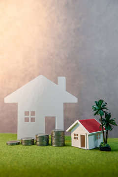 Real estate investment or Home mortgage loan rate. Property ladder concept. Coins stack, house model and table clock on green grass. Investment and business growth background