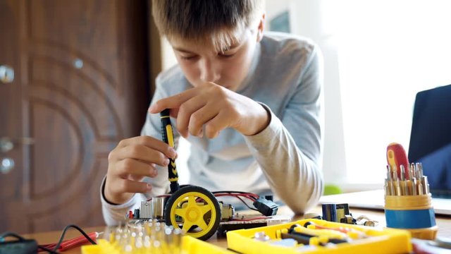 The boy designs an electronic toy model. Screws the missing screw in the circuit following the instructions. 4K video with shallow depth of field focus on hands.