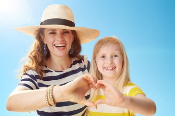 mother and daughter showing heart shaped hands against blue sky