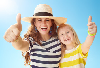 happy mother and daughter showing thumbs up against blue sky