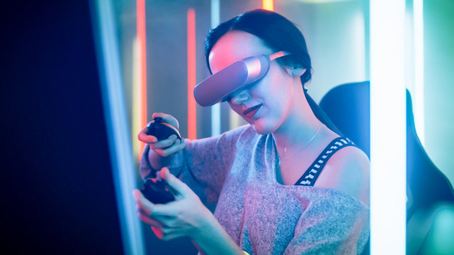 Pro Gamer Girl Wearing Virtual Reality Headset Plays Shooting Online Video Game with Joysticks / Controllers. Cool Retro Neon Colors in the Room.