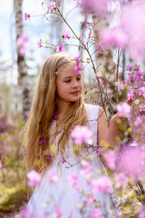 Fototapeta premium A child stands among the ledum and birch in white dress, smiling and fly hair