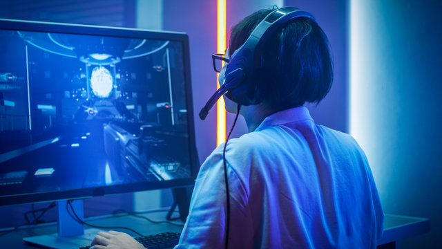 Professional Gamer Playing in First-Person Shooter Online Video Game on His Personal Computer. He's Talking with His Team Through Headset. Room Lit by Neon Lights in Retro Arcade Style. Cyber Sport.