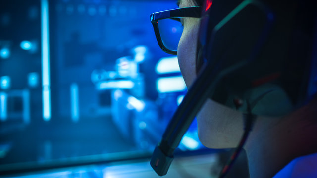 Close-up Shot of Professional Gamer Playing in First-Person Shooter Online Video Game on His Personal Computer. He's Talking with His Team Through Headset. Lit by Neon Lights in Retro Arcade Style.