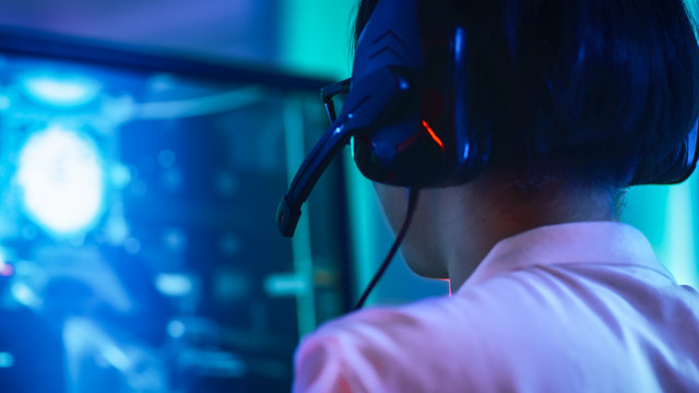 Close-up Portrait Shot of  the Professional East Asian Gamer Playing in Online Video Game on His Personal Computer. Talking into Microphone. Room Lit by Neon Lights in Retro Arcade Style. Cyber Sport.