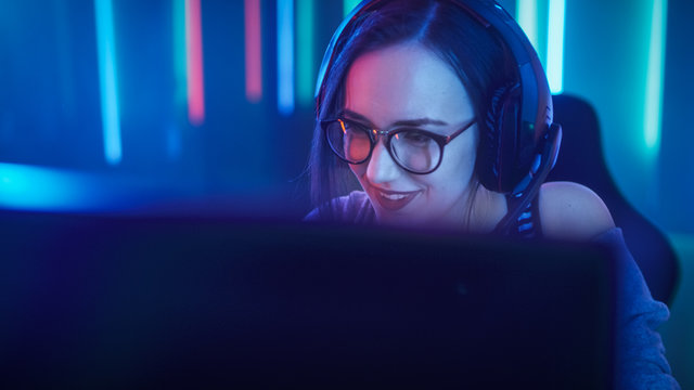 Beautiful Friendly Pro Gamer Girl Does Video Game Gameplay stream, Wearing Headset Talks / Chats' with Her Fans and Team into Headphones Microphone.Teenagers Having Fun. Neon Retro Colors.