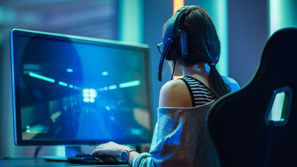 Shot of the Beautiful Pro Gamer Girl Playing in FPS Video Game on Her Personal Computer, Casual Cute Geek wearing Glasses and Headset. Neon Room. Online Cyber Games Internet Championship Event. - obrazy, fototapety, plakaty