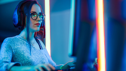 Portrait Shot of a Beautiful Professional Gamer Girl Playing in First-Person Shooter Online Video Game on Her Personal Computer. Casual Cute Geek wearing Glasses. Cyber e-Sport Internet.