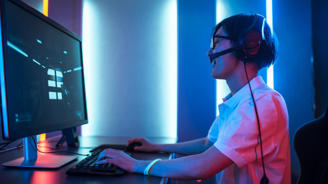 Side View Shot of Professional Gamer Playing in First-Person Shooter Online Video Game on His Personal Computer. He's Using Headset. Room Lit by Neon Lights in Retro Arcade Style. Cyber Sport.