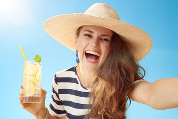 woman against blue sky with refreshing cocktail taking selfie