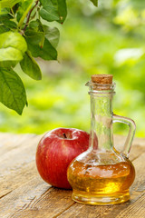 Apple vinegar in glass bottle and fresh red apple on wooden boar