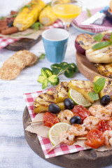 Picnic with grilled food. Sausages and corn on barbecue, shrimp, vegetables and fruits. Delicious summer lunch and plastic dishes. Top view