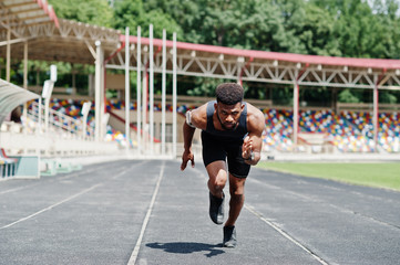 African american male athlete in sportswear racing alone down a running track at stadium.