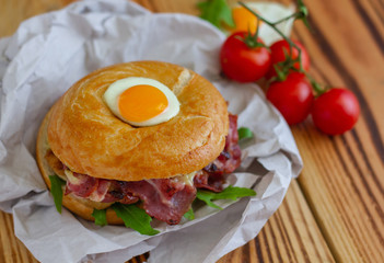 Bagel sandwich with turkey, bacon, ruccola, cheese, tomatoes and quail egg on the wooden background. Bagel burger.