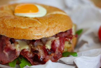 Bagel sandwich with turkey, bacon, ruccola, cheese and quail egg on the wooden background. Bagel burger.