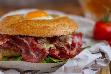 Bagel sandwich with turkey, bacon, ruccola, cheese, tomatoes and quail egg on the wooden background. Bagel burger with beer on the background