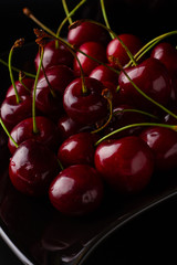 Cherries on black plate in form of heart. Cherry berry on a black background. Dark image of red cherries on a black reflective surface.
