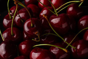 Bowl of cherries on a black background. Dark image of red cherries on a black reflective surface.