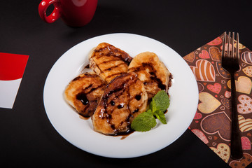 Pancakes with jam decorated with a mint leaf on a white plate on a black background. Photo in the studio