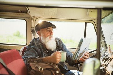 A senior hipster seated in his camper van looks at a road map 