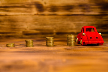 Stacks of the coins and red toy car on wooden table