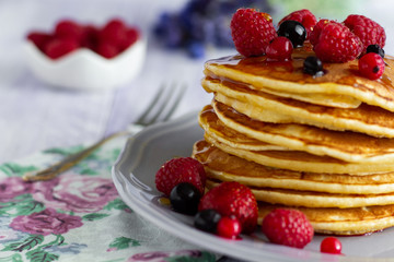 Stack of gold pancakes with berries and honey on wooden background