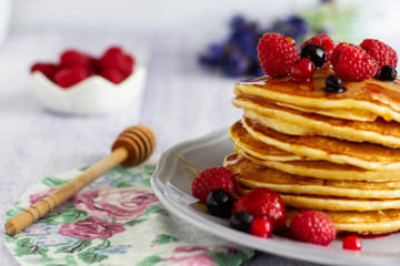 Stack of gold pancakes with berries and honey on wooden background
