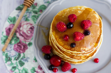 Stack of gold pancakes with berries and honey on wooden background