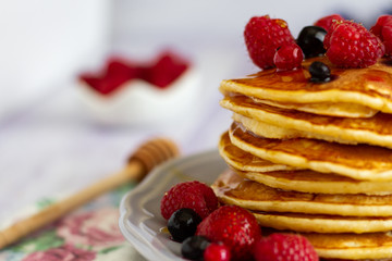 Stack of gold pancakes with berries and honey on wooden background