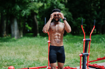 African american male athlete sexy sport bare torso man with running sports arm case for mobile phone, doing exercises on the street workout simulators.