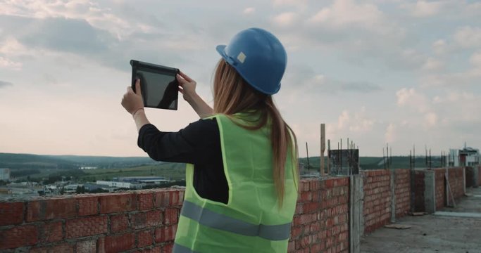 Woman architect at construction site using a tablet analyzing the building plan , background foreman s discussion something.
