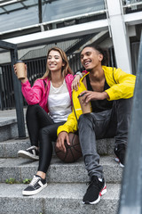 Obraz premium multiethnic couple with ball for basketball drinking coffee at city street