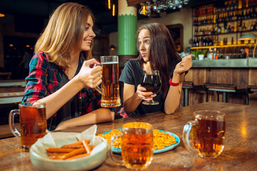 people, leisure, friendship and communication concept - happy friends drinking beer, talking and clinking glasses at bar or pub