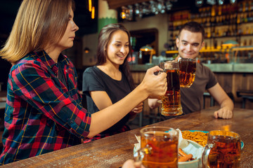 people, leisure, friendship and communication concept - happy friends drinking beer, talking and clinking glasses at bar or pub