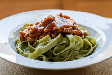 Primer plano de un plato de tallarines de espinaca con carne y salsa de tomate a lo boloñesa en un plato blanco con orégano ara decorar