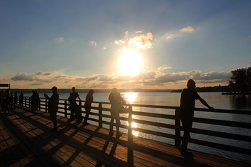 Menschen beobachten am Bootssteg den Sonnenuntergang am Ammersee