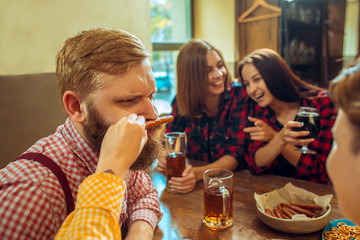people, leisure, friendship and communication concept - happy friends drinking beer, talking and clinking glasses at bar or pub