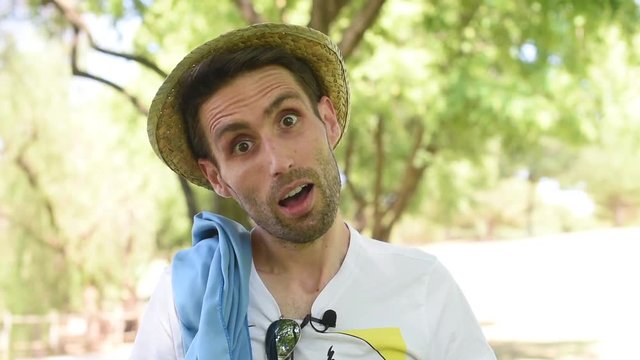 Hombre joven con sombrero y toalla en la naturaleza abriendo la boca sorprendido