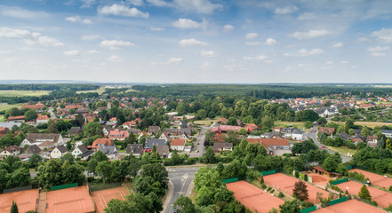 Obraz premium Widok z lotu ptaka z przedmieścia niemieckiego miasta z szerokim widokiem po horyzont, kort tenisowy i domy jednorodzinne na przedmieściu.