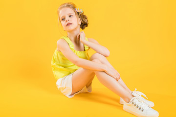 A teenage girl is sitting on a yellow background.