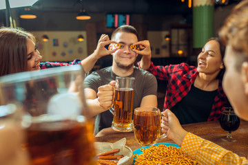 people, leisure, friendship and communication concept - happy friends drinking beer, talking and clinking glasses at bar or pub