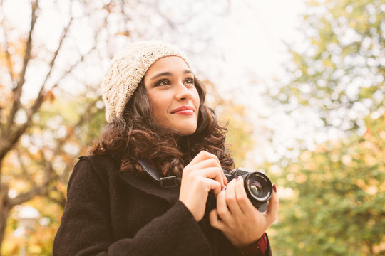 Young beautiful woman with a woolen cap taking pictures with a retro camera in the city in autumn