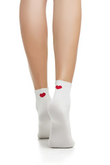 Cropped back view of beautiful female legs in white socks with red heart prints, isolated against a white background. The young woman making a step forward. Comfortable legwear for ladies and girls.