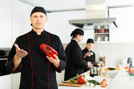 Professional chef  in black uniform standing  with big red  pepper