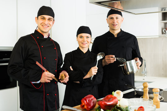 Three young cooks wearing black uniform showing thumbs up