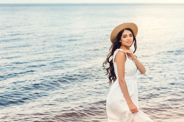 Fototapeta na wymiar attractive girl in straw hat walking near the sea in summer