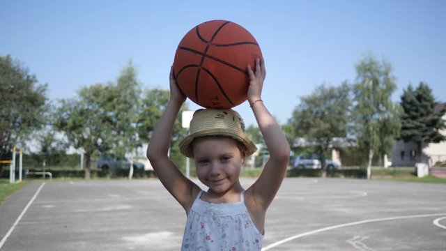Little child girl portrait stay posing holding a basketball ball over her head on playground
