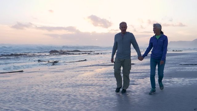 Senior couple walking at sunset on a sandy beach 
