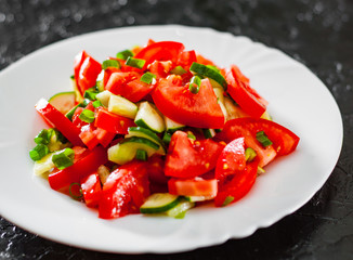 fresh vegetable salad with tomato, cucumber and green onion in white plate on black background.
