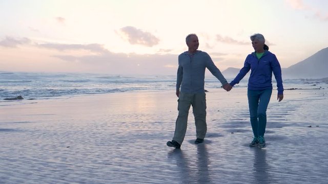 Senior couple walking at sunset on a sandy beach 
